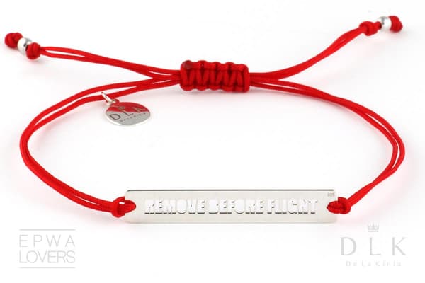 Rött snörearmband med utskuren text "Remove Before Flight"